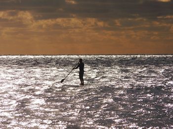 Silhouette man fishing in sea against sky during sunset