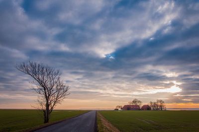 Road amidst field against sky during sunset