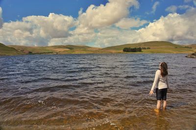 Rear view of woman standing in lake against cloudy sky