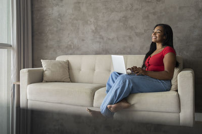 Young black woman working at home with laptop on her lap sitting on her couch  notebook for working. 