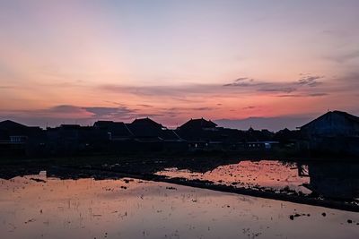 Scenic view of lake by buildings against sky during sunset