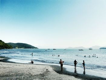 People on beach against clear blue sky