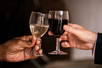 Hands of a black and a white person toasting with glasses of red and white wine