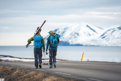 A couple walks down a road in iceland holding ski gear