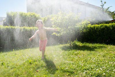 Full length of shirtless boy playing with water at yard on sunny day