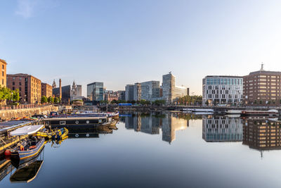 Boats moored in river by buildings against clear sky