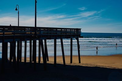 Silhouette pier on beach against sky