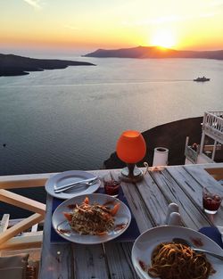 Food served on table at balcony by sea against sky during sunset