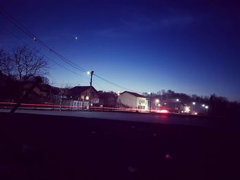 Illuminated road against clear blue sky at night