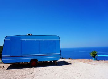 Blue caravan on field by sea against sky