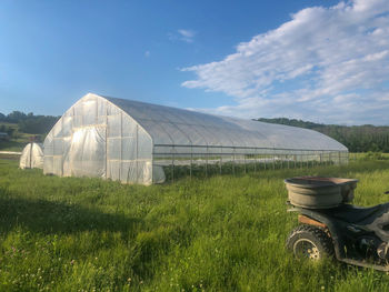 Scenic view of agricultural field against sky with greenhouse and off road vehicle