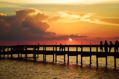 Silhouette people on pier over sea against sky during sunset