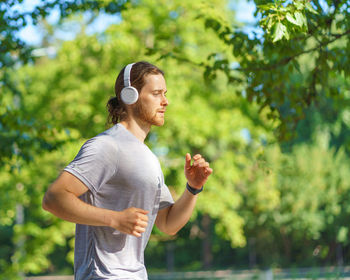 Young male sportsman wearing headphones jogging in green park in morning