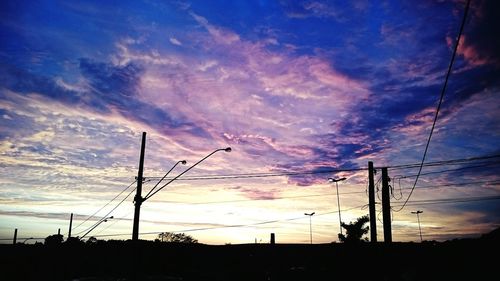 Silhouette electricity pylons against dramatic sky