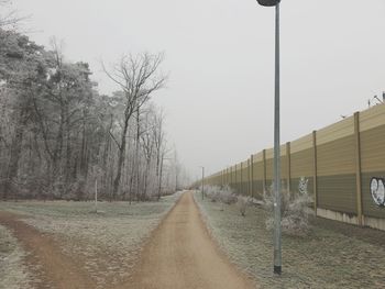 Road amidst trees on field against sky during winter