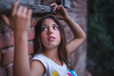 Young woman looking up while standing against brick wall