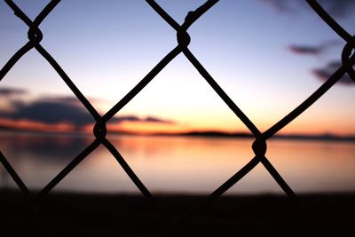 Close-up of chainlink fence against sky during sunset