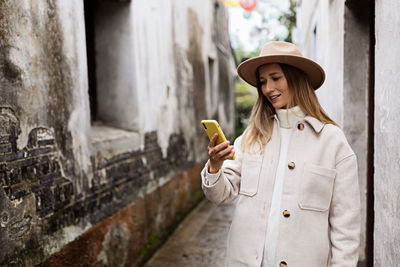 Young woman holding apple while standing against wall