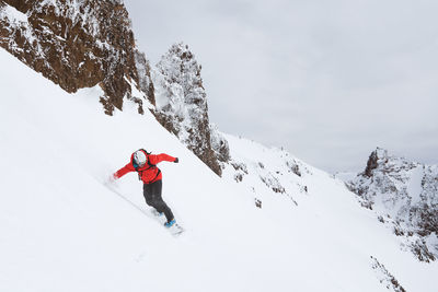 Snowboarder riding down mountain in red jacket