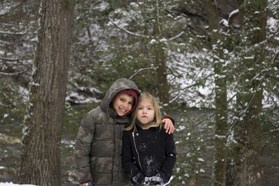 Portrait of happy brother standing with sister against trees during winter