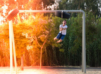 Cheerful boy swinging at playground during sunny day