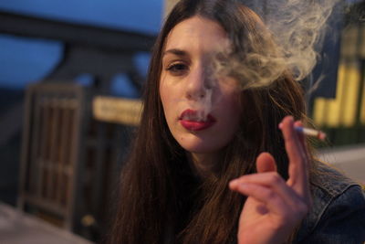 Close-up of young woman smoking cigarette in city at night