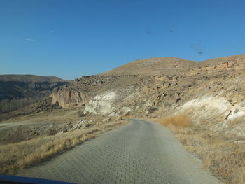 Road leading towards mountains against clear blue sky