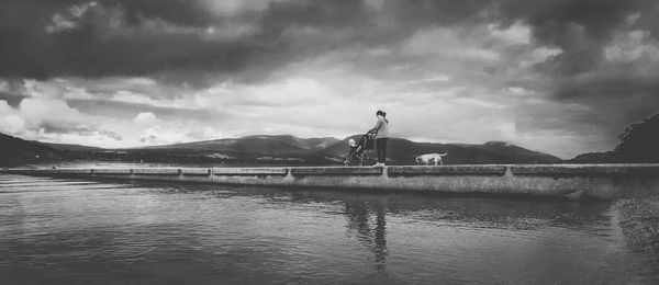 Scenic view of lake with woman and baby on pier against sky