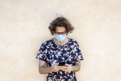 Young man wearing mask using smart phone against wall