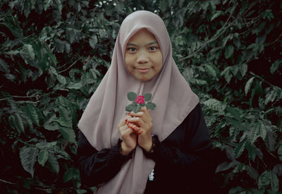 Portrait of young woman standing against plants