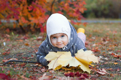 Cute little girl is lying on a grass with yellow maple leaves on a walk in autumn park.