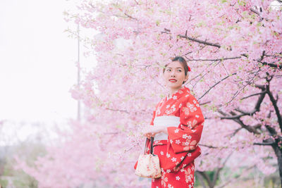 Low angle view of woman standing by pink cherry blossom tree