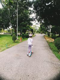 Rear view of girl playing with push scooter on footpath