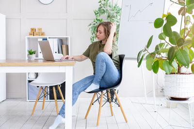 Young woman using phone while sitting on table at home