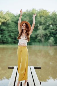 Rear view of woman with arms raised standing against lake