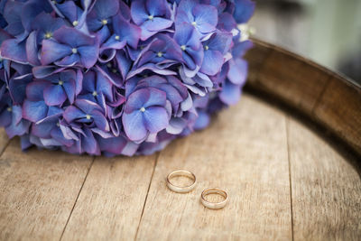 High angle view of wedding rings by purple flowers on wooden table