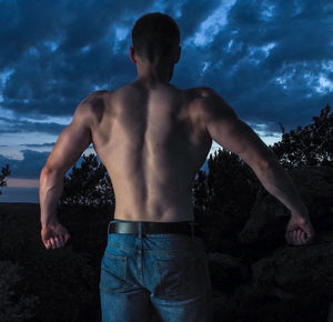 Rear view of shirtless man standing against sky