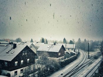 Railroad tracks by houses against sky during snowfall