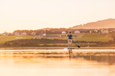 Man standing in lake against sky during sunset