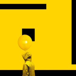 Person wearing yellow jacket with balloon standing by painted wall