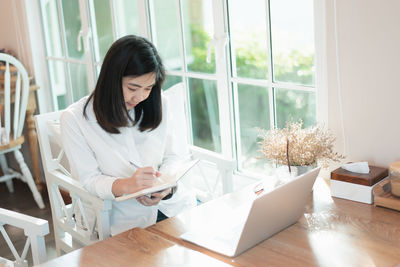 Young woman using phone while sitting on table