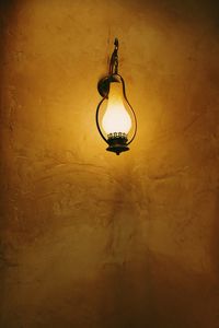 Low angle view of illuminated light bulb hanging on wall