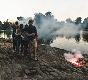 Rear view of people standing by lake against sky