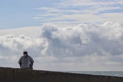Rear view of man sitting against cloudy sky