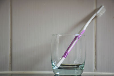 Close-up of toothbrush in drinking glass against tiled wall