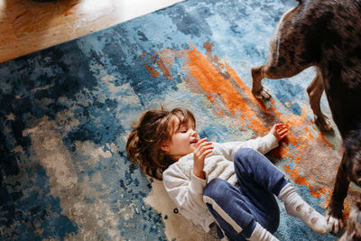 Upper view of child playing with dog lying on the carpet at home