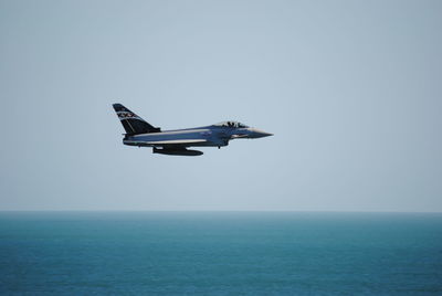 Military airplane flying over sea against sky