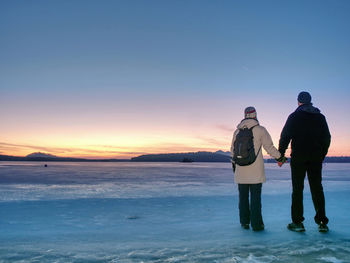 Couple has fun during winter walk on ice of frozen lake. evening hike at beach of pond. warm clothes