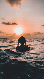 Silhouette men in sea against sky during sunset