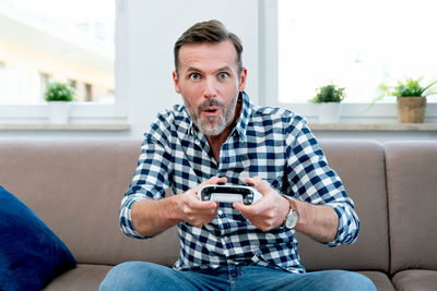 Portrait of young man using phone while sitting on sofa at home